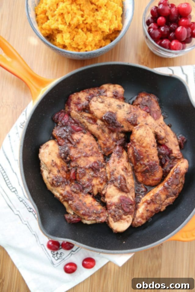 chicken in skillet covered in cranberry balsamic sauce next to container of cranberries