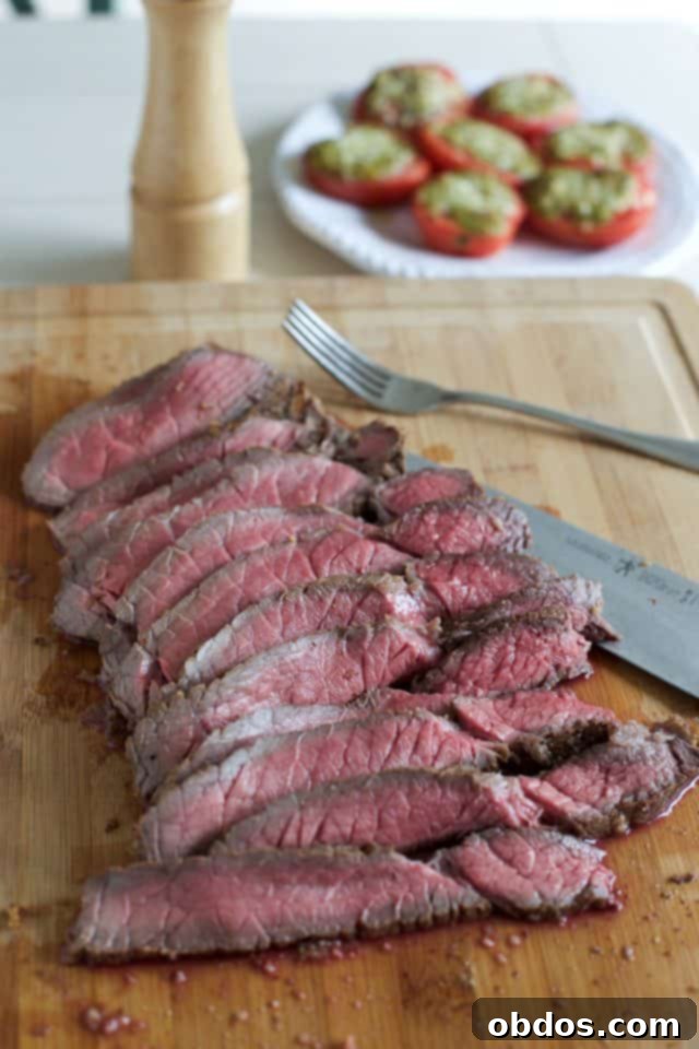 Κομμάτια London Broil σε ξύλο κοπής, κομμένα λεπτά, με ψητές ντομάτες πέστο στο παρασκήνιο