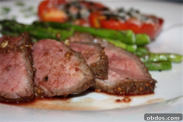 Κομμένα κομμάτια London Broil σε λευκό πιάτο με σπαράγγια και ντομάτες στο παρασκήνιο