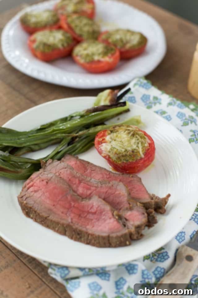 Λευκό πιάτο με κομμένη μπριζόλα London Broil, φρέσκο κρεμμυδάκι και ψητές ντομάτες με παρμεζάνα στο παρασκήνιο